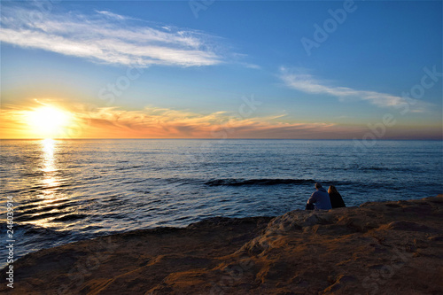 Couple sitting on a cliff at sunset © Kimberly