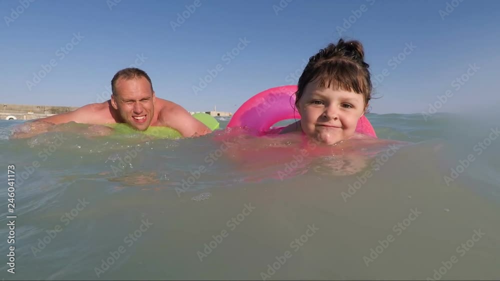 Family at sea. A little girl swims with her dad in the sea on rubber rings. Family at sea. A little girl swims with her dad in the sea on rubber rings.