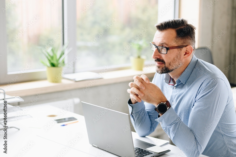 Middle aged handsome businessman in shirt working on laptop computer in office