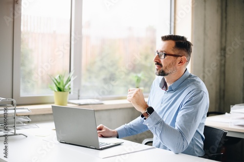 Middle aged handsome man in shirt working on laptop computer in office