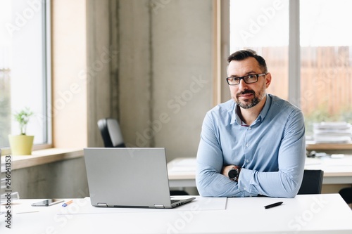 Middle aged handsome man in shirt working on laptop computer in office