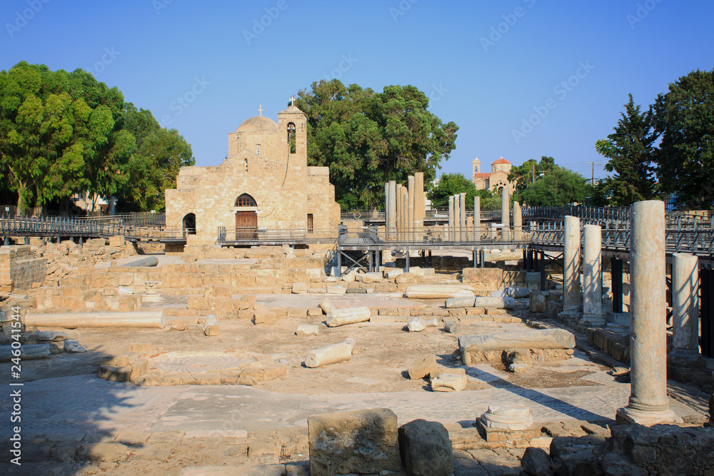 A large white church with a bell tower in ancient ruins in the midst of ancient columns on the island of Cyprus