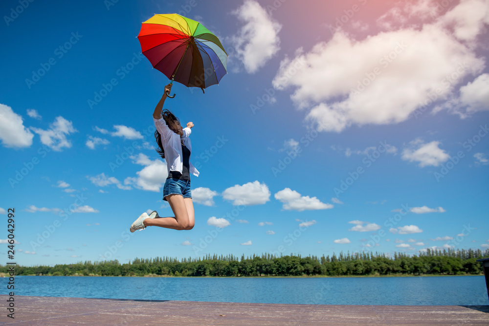 Young happy woman holding full color umbrella jumping in the air expressing happiness. Relaxed atmosphere, summer.
Young happy woman holding full color umbrella jumping in the air expressing happiness. Relaxed atmosphere, summer.