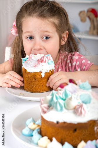 Studio shot of small  girl  sitting at a table and eating Easter cakes.