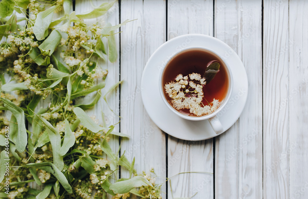 White cup of linden tea on linden blossom background. Herbal medicine. Top view. Treatment of cold and flu concept. White cup of linden tea on linden blossom background. Herbal medicine. Top view. Treatment of cold and flu concept.