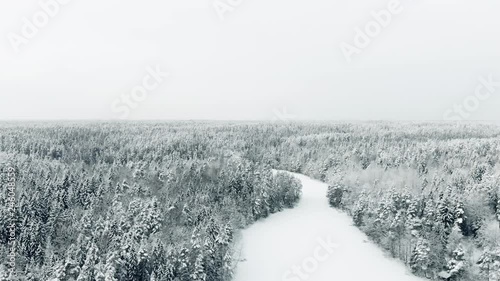 Aerial, tilt down, drone shot, above Haukkalampi pond, surrounded by snow, covered trees and endless, winter forest, on a overcast day, in Nuuksio national park, in Finland photo