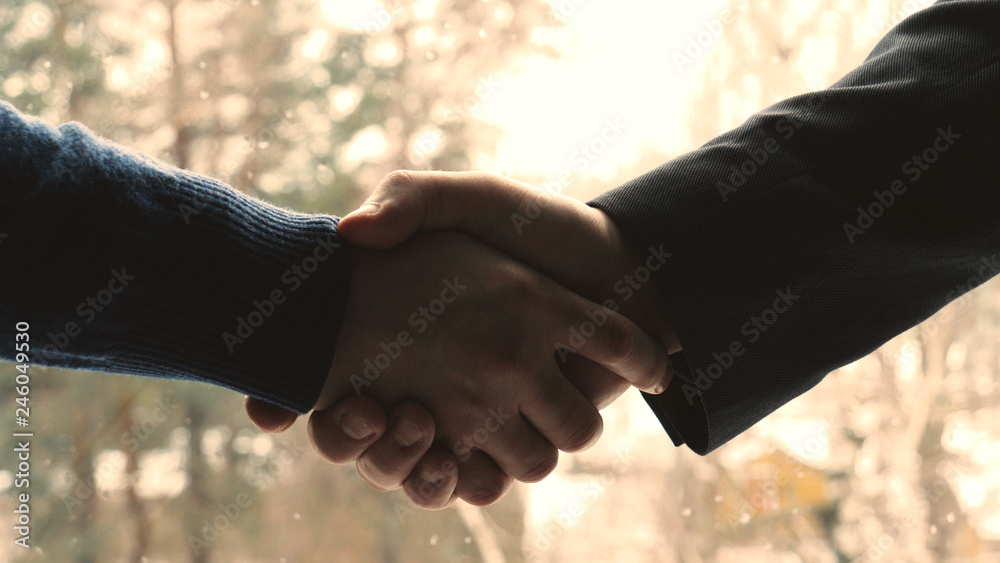 Two young men (guys), businessmen, shaking hands, greeting each other at a meeting in a building (office) against the background of the street. Concept of: Business meeting, Very Close, Important Meet