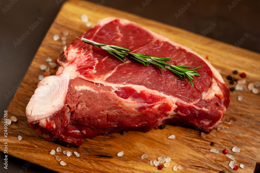 Raw meat steak with seasoning on a cutting board, background concrete. . Beef T-bone steak, top view. Barbecue concept. Ingredients for roasting meat. Raw meat steak with seasoning on a cutting board, background concrete. . Beef T-bone steak, top view. Barbecue concept. Ingredients for roasting meat.