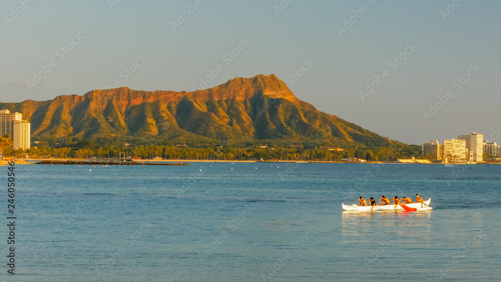 boys paddle an outrigger canoe at waikiki beach with diamond head in the distance