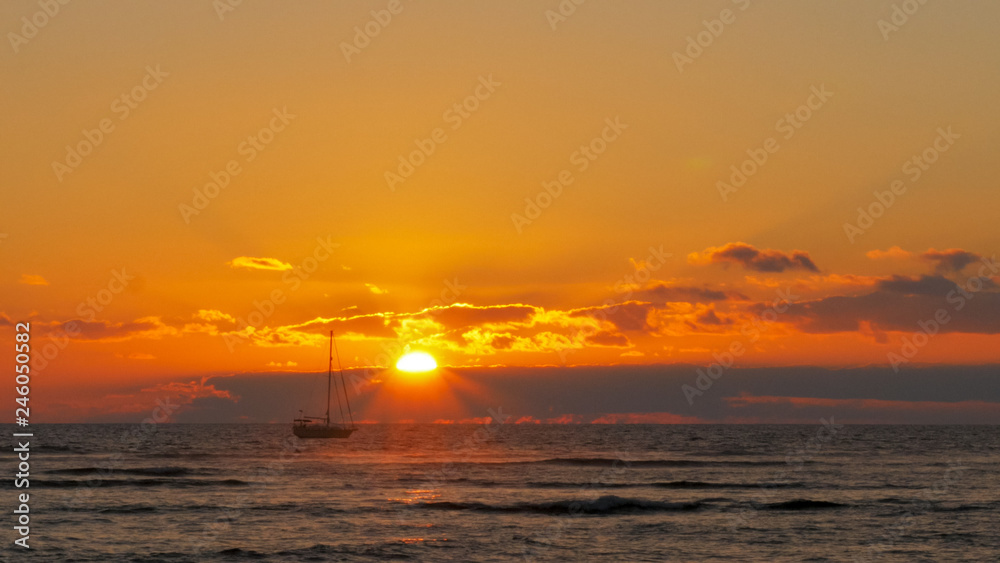 yacht sails past the setting sun at waikiki