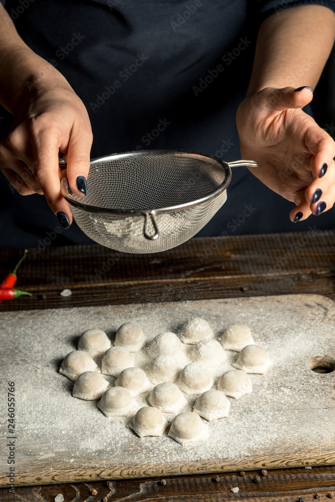 Uzbek national food Chuchvara, like dumplings, lie in the shape of a heart, on a wooden board, hands are crushing flour from above Uzbek national food Chuchvara, like dumplings, lie in the shape of a heart, on a wooden board, hands are crushing flour from above