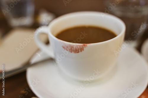 Close up of red lipstick smudges on hot latte in white coffee cup on wood table near window in coffee shop in the morning in vintage soft tone, metaphor of female office worker