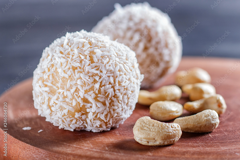Energy balls cakes with coconut and cashew on wooden board on black background.