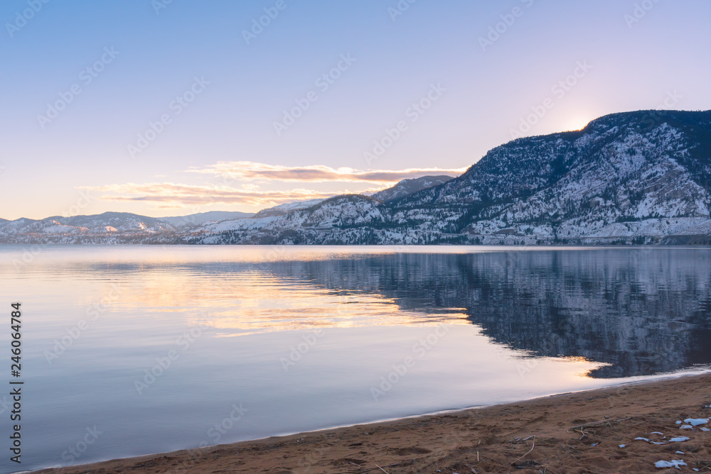 Beach with calm water, view of snow covered mountains and sunset sky