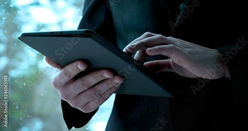 A man (guy) in a suit in a office building on the background of the street is holding a tablet. Concept from: Waiting, Meeting, Marketing, Making a meeting, Looking at a tablet, Writing a message.