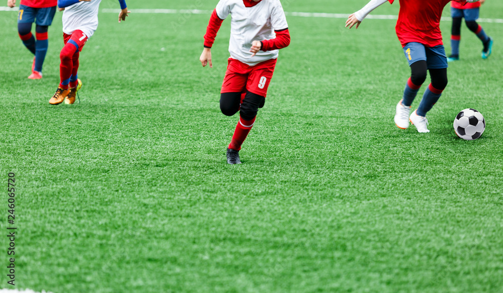 Boys in red and white sportswear plays soccer on green grass field. Youth football game. Children sport competition, kids plays outdoor, activities, training Boys in red and white sportswear plays soccer on green grass field. Youth football game. Children sport competition, kids plays outdoor, activities, training
