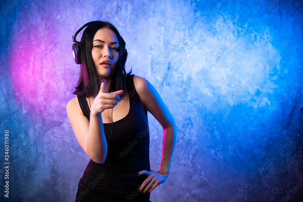 Smiling woman wearing headset with microphone looking pointing finger at camera you on neon colored background