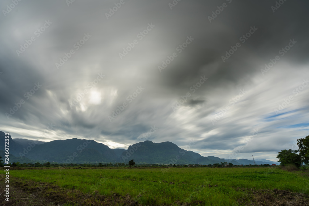 Obraz premium Paddy rice field with storm clouds and Doi Nang Non Mountains background in Chiangrai Thailand