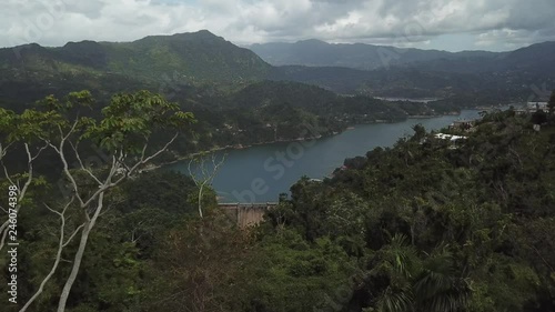 AERIAL: pushing past a skinny tree to reveal a dam and lake between the mountain tops of Utuado, Puerto Rico. photo