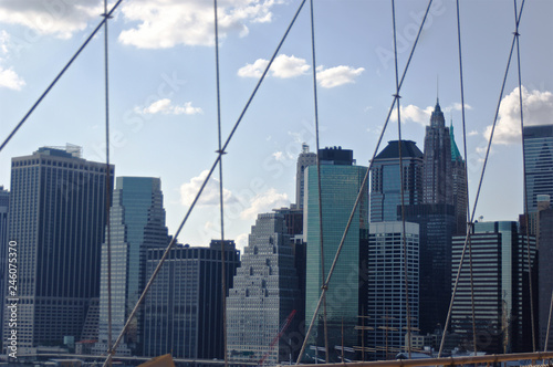 A cluster of buildings situated in New York City's lower Manhattan as seen through the high-tension wires of the iconic Brooklyn Bridge.