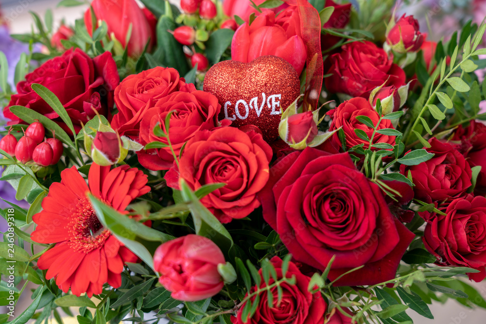 a festive bouquet of a variety of red flowers and a heart with the inscription love for Valentine's day and other holidays a festive bouquet of a variety of red flowers and a heart with the inscription love for Valentine's day and other holidays