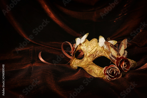 Photo of elegant and delicate gold venetian mask over dark silk background.