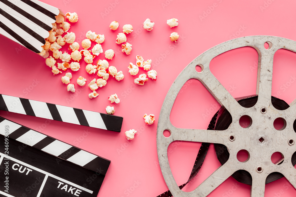 Movie premiere concept. Clapperboard, film stock, popcorn on pink background top view