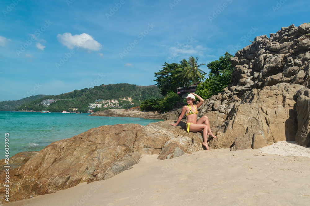 Young happy woman in swimsuit and hat is resting on the beach in Thailand.
