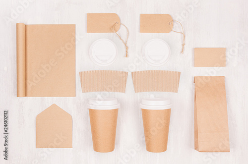 Coffee shop template for branding identity - two brown paper cups with blank notebook, packet, label, card, cap, envelope on white wood board, top view.