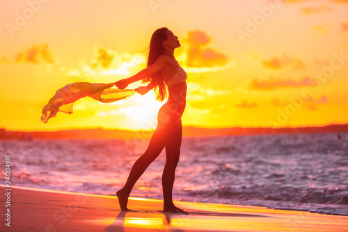Sexy woman silhouette feminine curves bikini body swimsuit lady with scarf flying in the wind at sunset glow flare for weight loss sensuality concept. Sun vacation travel beach.