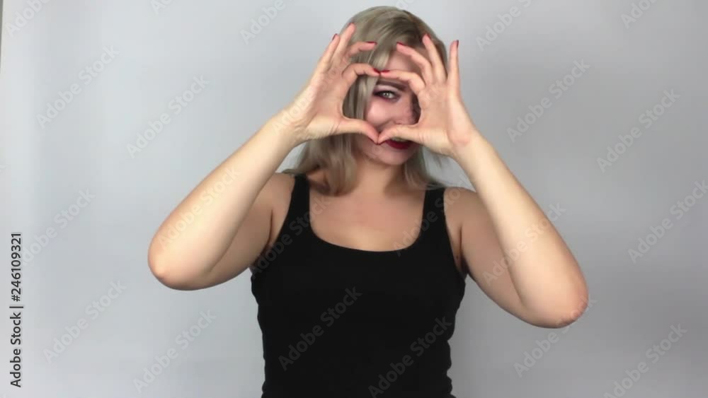 A blond woman in a black T-shirt makes a heart sign and sends an air kiss, on a white background in the studio A blond woman in a black T-shirt makes a heart sign and sends an air kiss, on a white background in the studio
