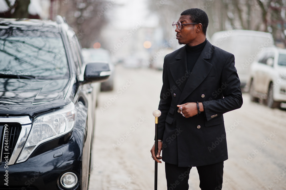 Stylish african american gentleman in elegant black jacket, holding retro walking  stick as cane flask with golden diamond ball handle. Rich fashionable afro  man against business suv car. Stock Photo | Adobe