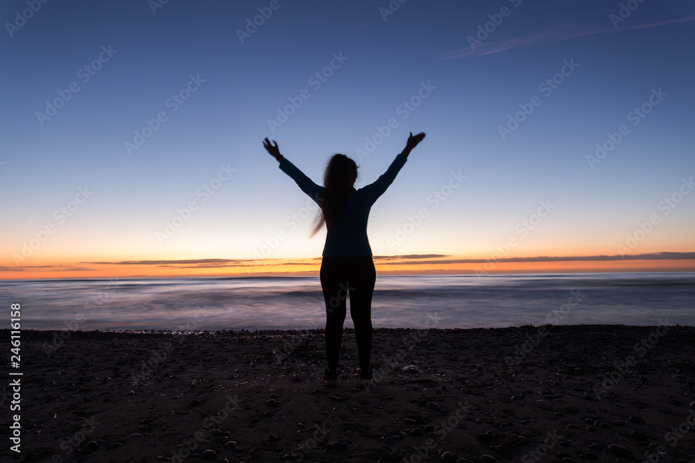 Freedom, holiday and victory concept - Silhouette of woman with hands up while standing on the sea beach at sunset