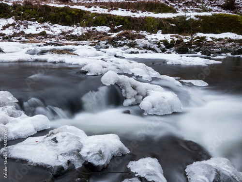 smooth motion of wild water in a river in winter with snow and ice on rocks and stones in the beautiful nature of a forest