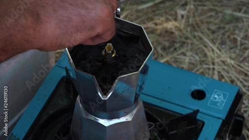 A close up of a man�s hand lifting the lid and stirring a Moka coffee pot over a camping stove on the ground. photo