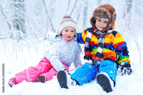 Two cute little kids boy and girl in winter snowy forest at snowflakes background. outdoors leisure and lifestyle with children on cold snowy days. Happy siblings, brother and sister playing