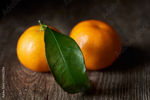 selective focus of green leaf on organic tasty tangerine on wooden table