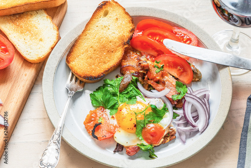 Fresh rustic breakfast - fried egg with bacon, onion and tomatoes on a plate  and toast on a light wooden background, close-up