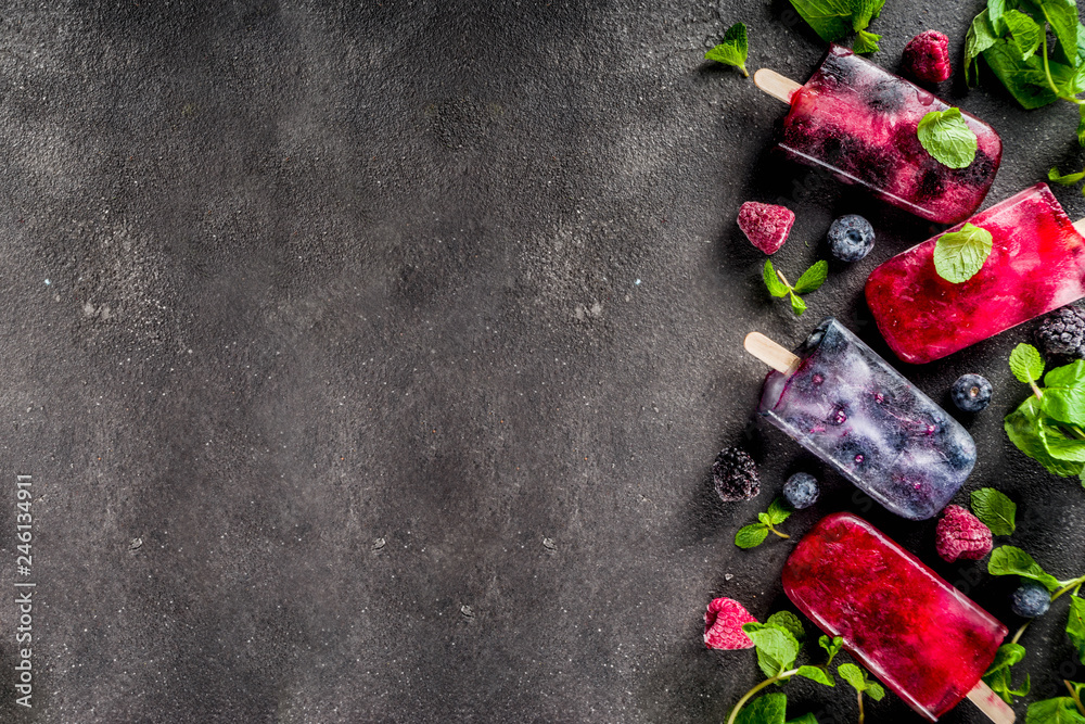 Simple and healthy summer dessert. Homemade berry ice cream popsicles with mint. Mojito lollypops, frosen diet infused water with blackberry, blueberry and raspberry. Dark concrete background copy spa
