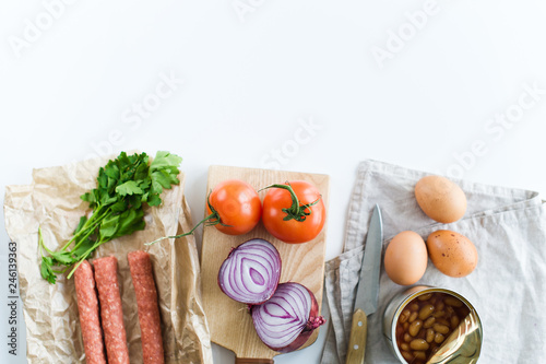 English Breakfast. Ingredients sausages, canned beans, parsley, dill, bread, tomatoes, bacon, onions and eggs. The view from the top. Space for text. White background