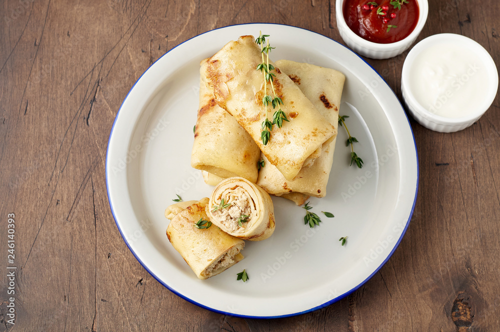 Savory crepe rolls with ground meat filling served with sour cream and tomato sauce Savory crepe rolls with ground meat filling served with sour cream and tomato sauce