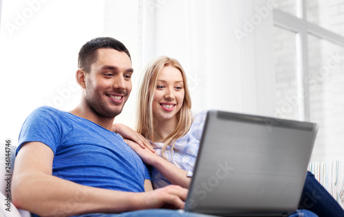 technology, internet and people concept - happy couple with laptop computer at home