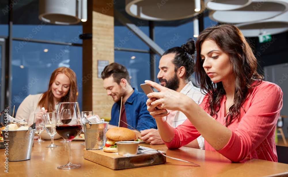 technology, lifestyle and people concept - bored woman dining with friends and messaging on smartphone at restaurant