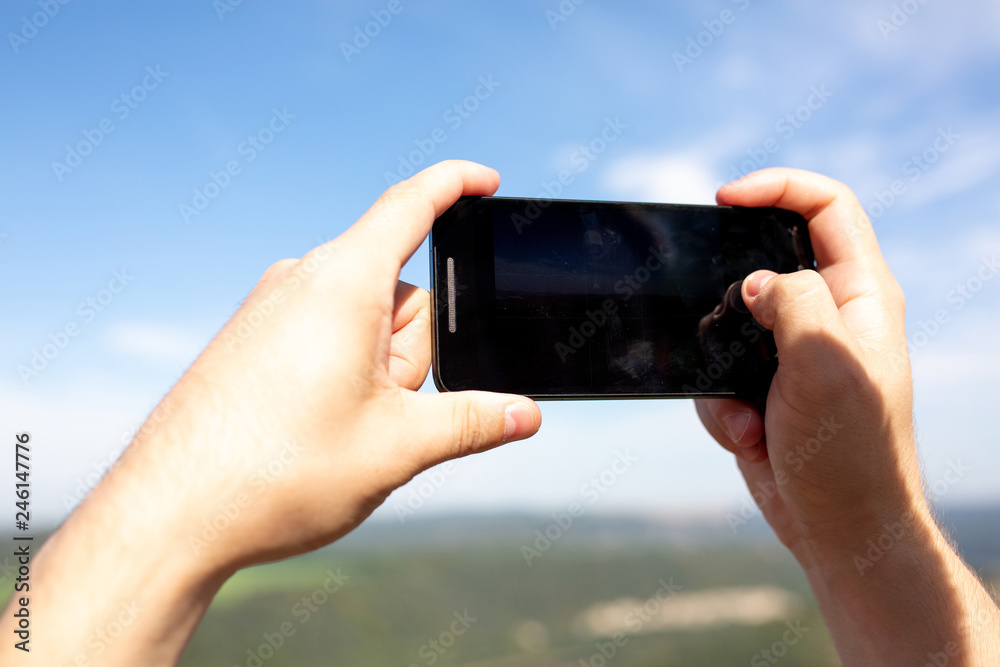 Male hands holding his smart phone outdoor, records video in the landscape park