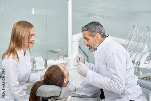 Doctor and assistant working with client in dentist cabinet.