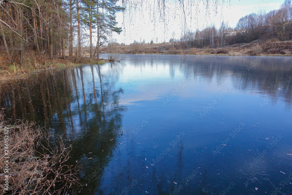 Blue ice on the surface of a forest lake. The snow has not yet fallen. Early winter