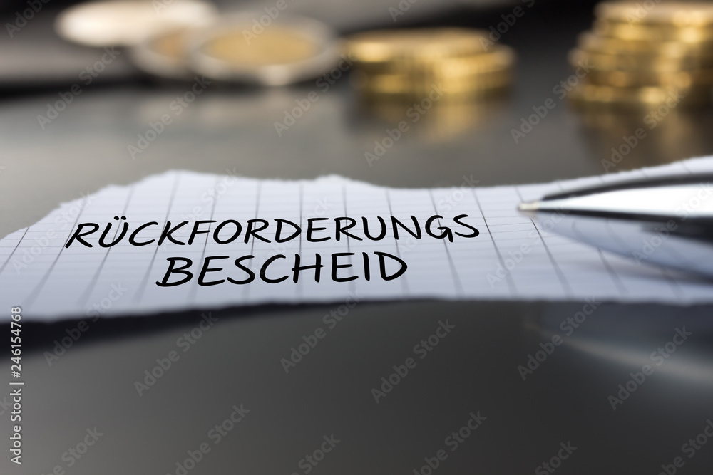 Rückforderungsbescheid auf einem Zettel mit Stift vor Geldmünzen Rückforderungsbescheid auf einem Zettel mit Stift vor Geldmünzen