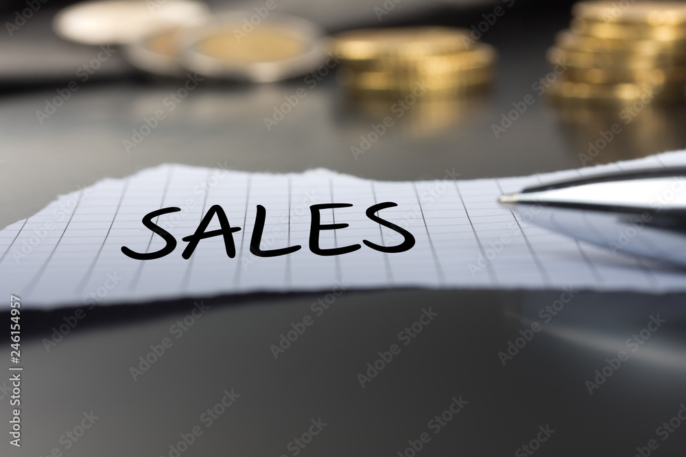 Sales auf einem Zettel mit Stift vor Geldmünzen Sales auf einem Zettel mit Stift vor Geldmünzen