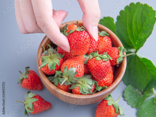 A young woman is holding a bowl of strawberries isolated on a airy blue background, closeup, topview, copyspace.