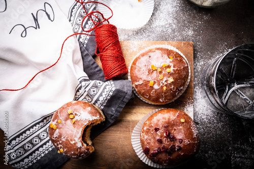 Pączki z lukrem i skórka pomarańczową. Apetyczne słodkie ciastka na kuchennym stole.